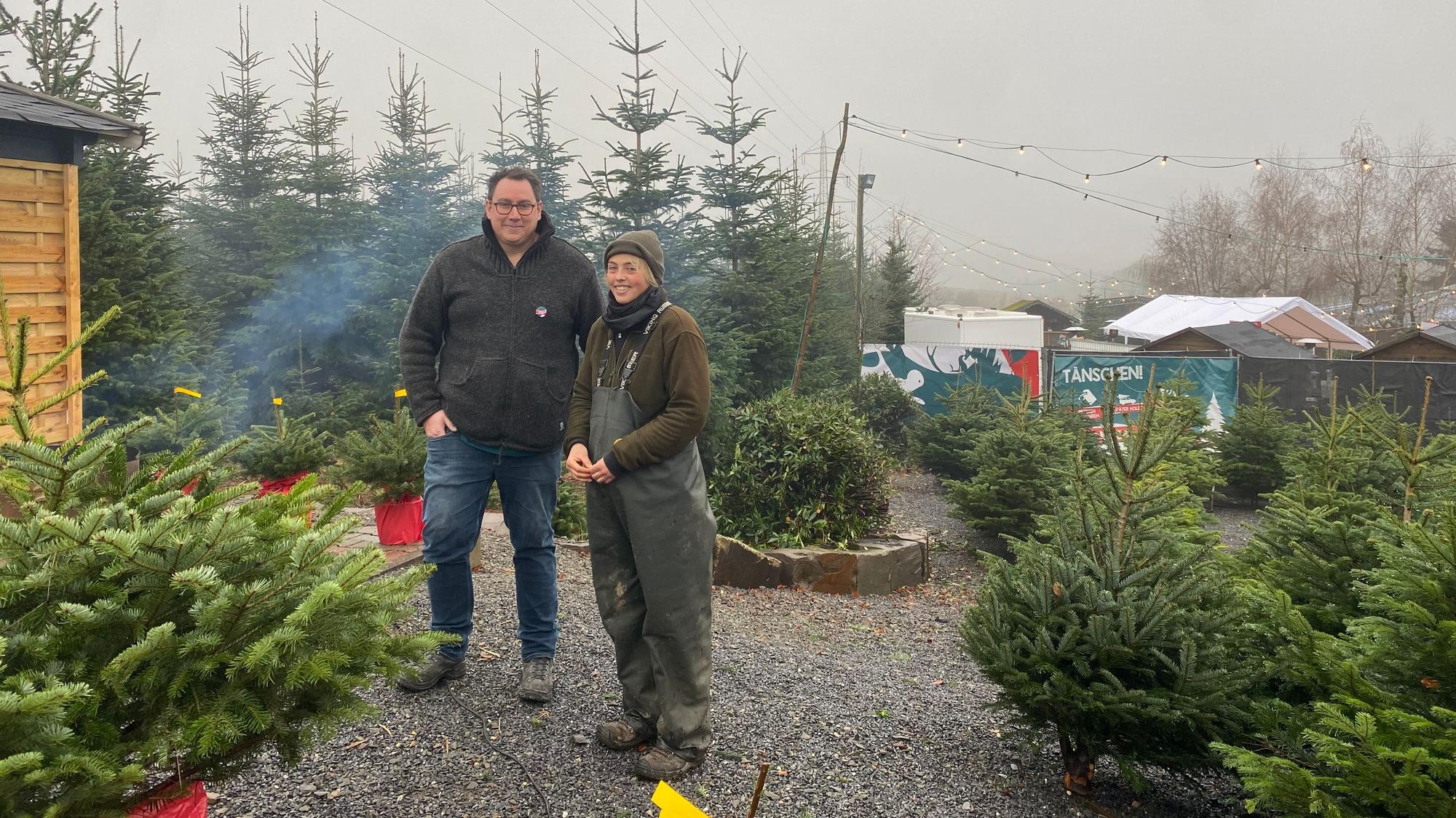 Christian Hoffmann, Organisator des Weihnachtsmarkts und Regina Coßmann, Mitarbeiterin der Baumschule Mütherich, stehen zwischen Tannen.