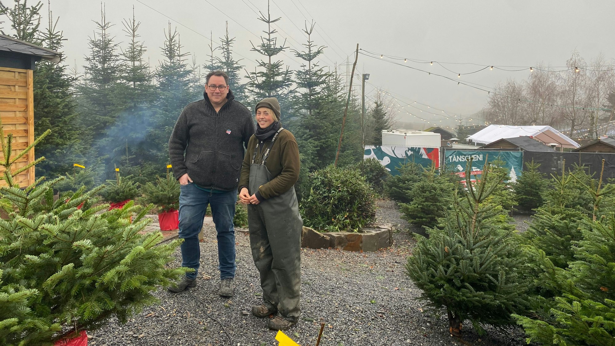 Christian Hoffmann, Organisator des Weihnachtsmarkts und Regina Coßmann, Mitarbeiterin der Baumschule Mütherich, stehen zwischen Tannen.