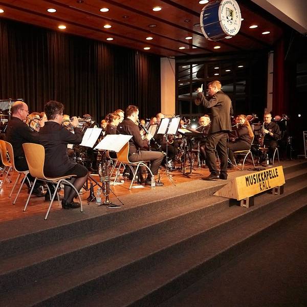 Die Aktiven der Musikkapelle Kall sitzen auf der Bühne der Aula in Steinfeld und geben ein Konzert.