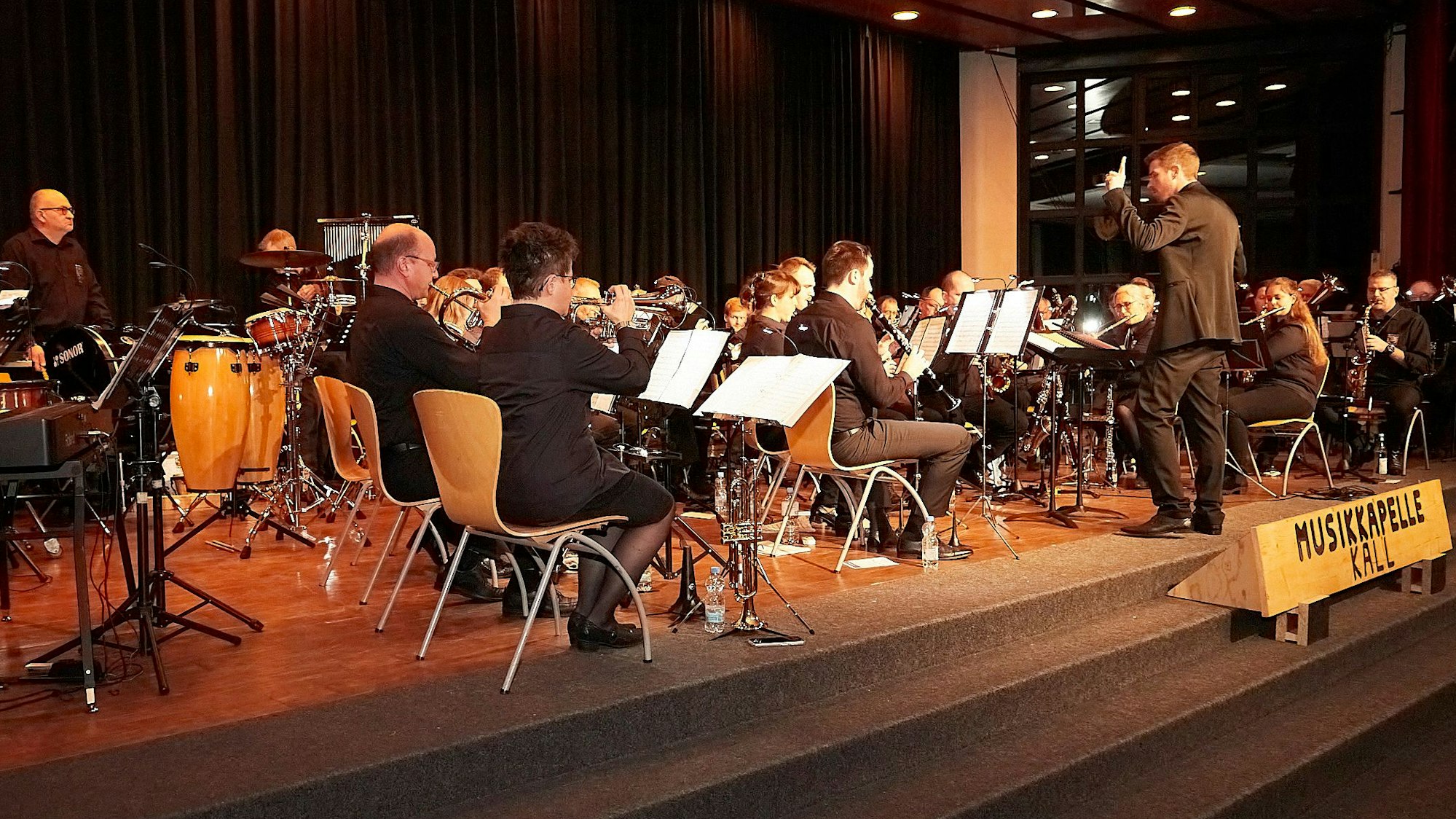 Die Aktiven der Musikkapelle Kall sitzen auf der Bühne der Aula in Steinfeld und geben ein Konzert.