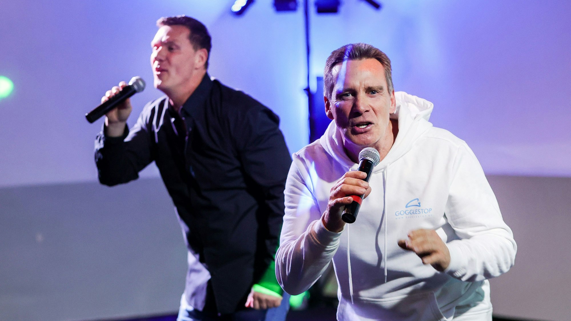 Jürgen und Peter Milski, in Hemd und Hoodie, singend mit Mikros in der Hand.