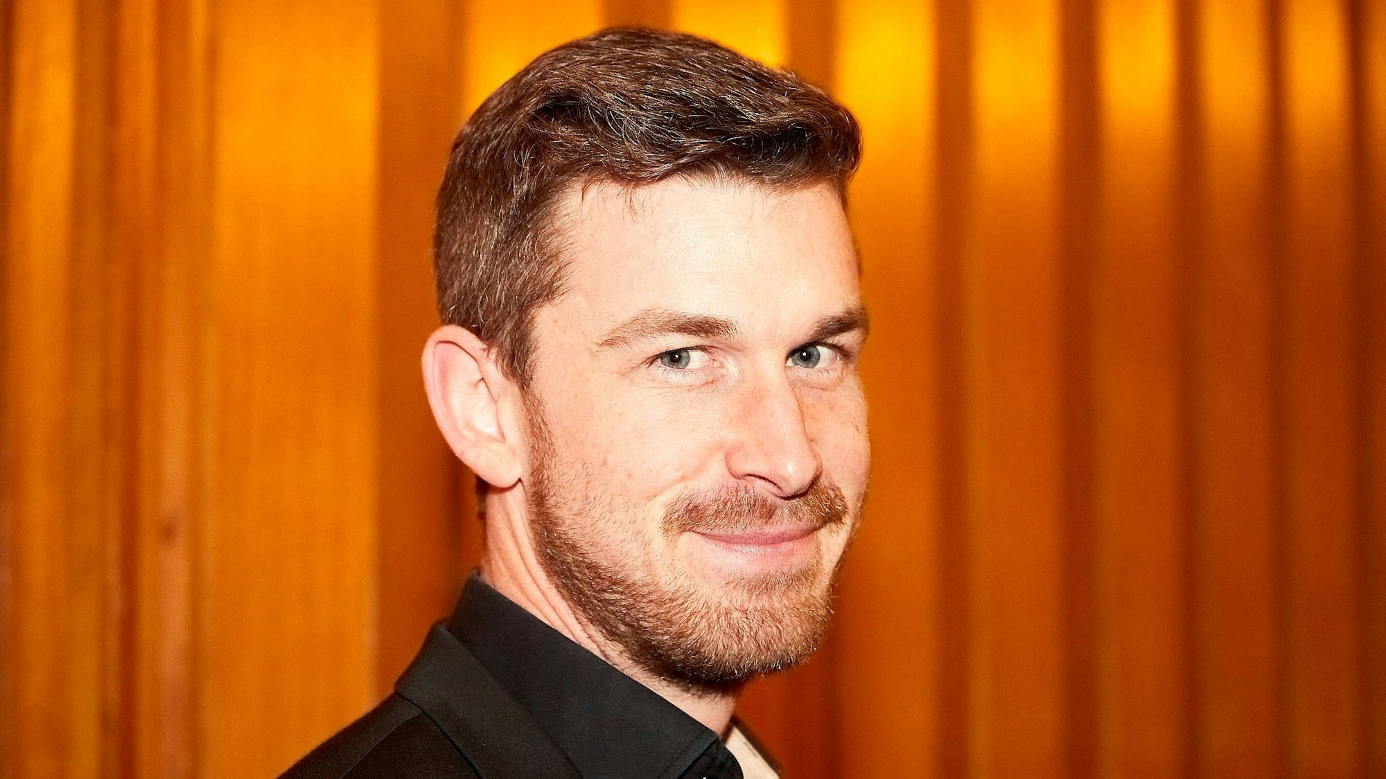 Das Porträt zeigt Marco Leibach, den neuen Dirigenten der Musikkapelle Kall. Er steht vor einer hölzernen Wand.