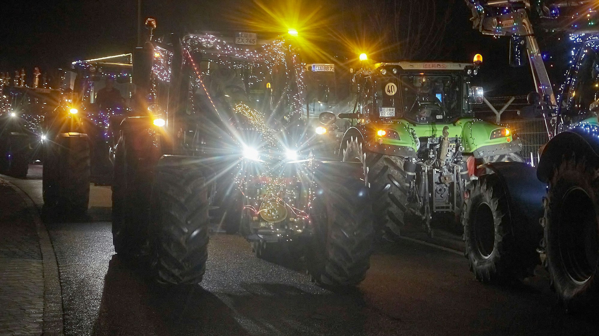 Bunt beleuchtete Traktoren fahren im Dunkeln über eine Straße.
