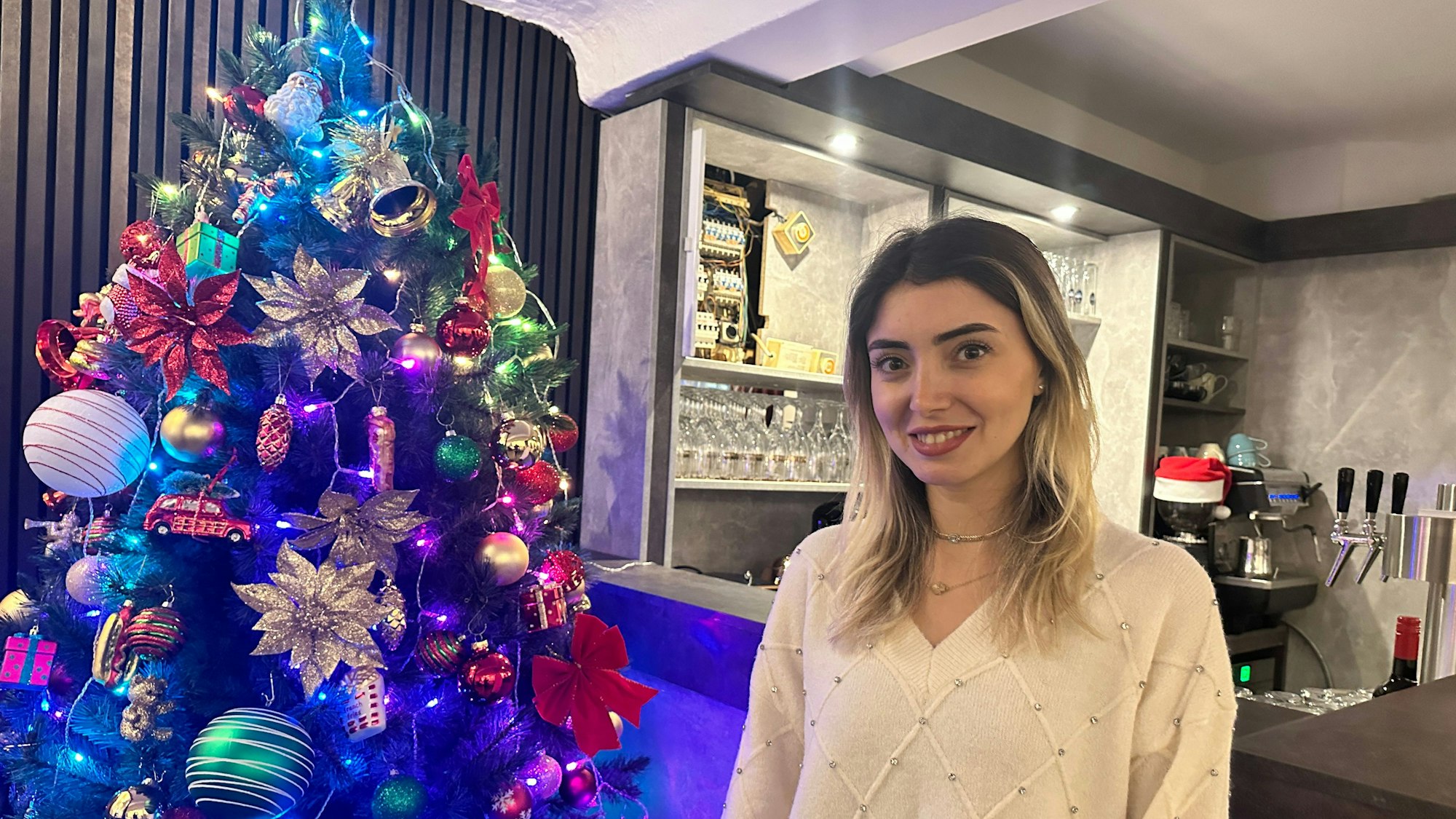 Eine Frau mit blonden offenen Haaren steht in einem Lokal neben einem Weihnachtsbaum.