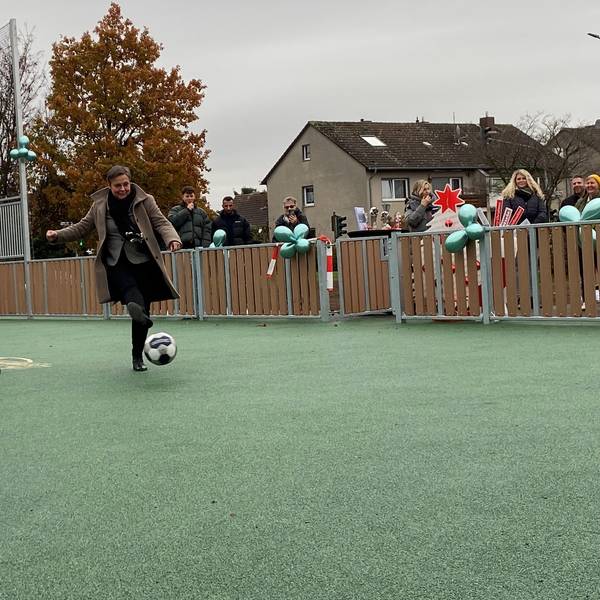 Auf einem Tartan-Platz kickt Schulleiterin Karin Bossant unter den Augen des Bürgermeisters Sacha Reichelt einen Fußball.
