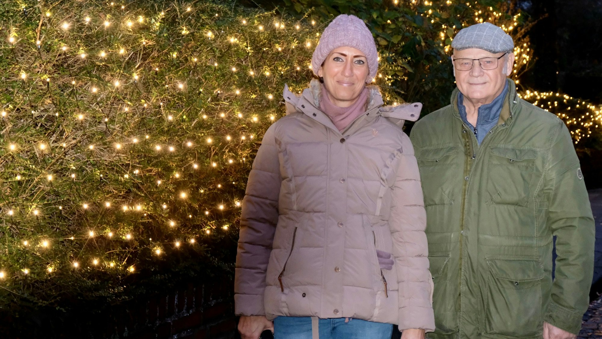 Eine Frau und ein Mann stehen vor einer lichtergeschmückten Hecke.