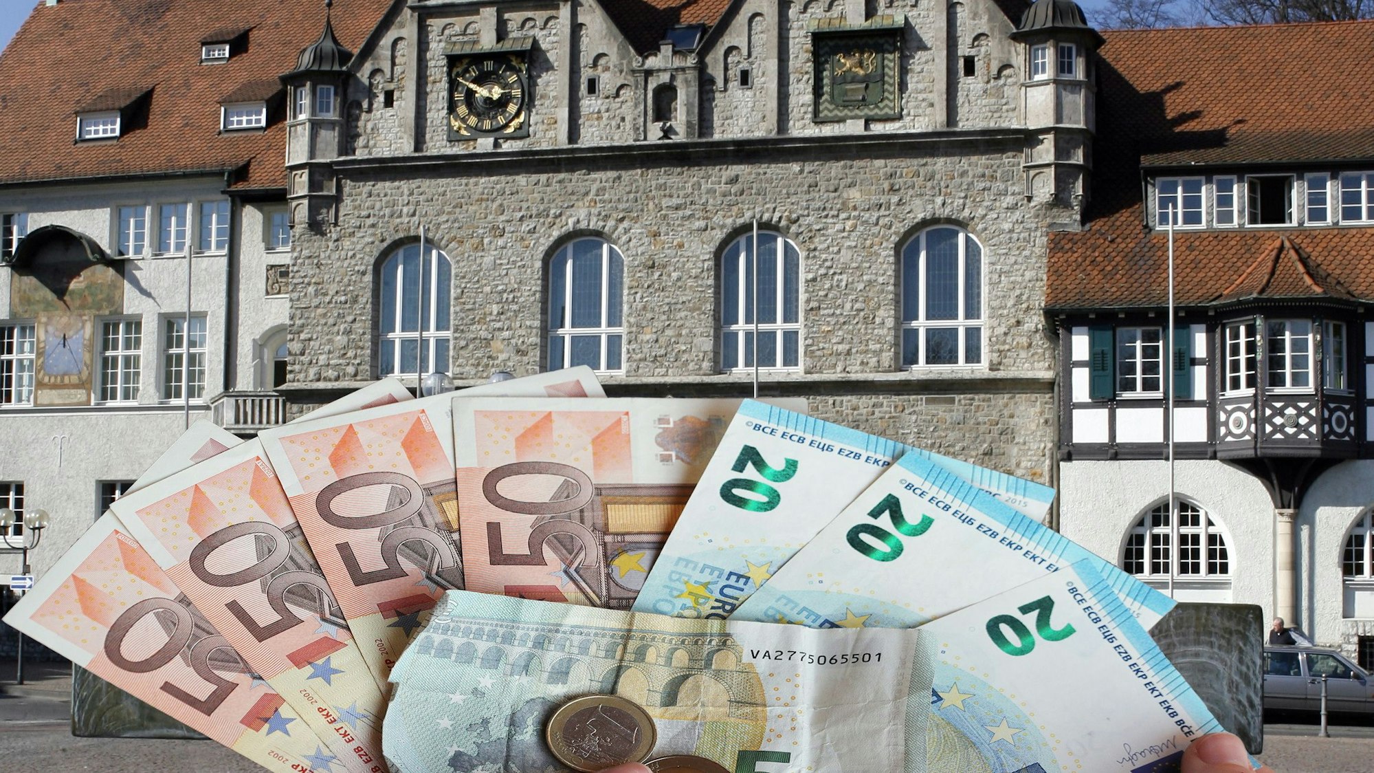 Geldscheine werden hochgehalten. Im Hintergrund ist das Bergisch Gladbacher Rathaus.