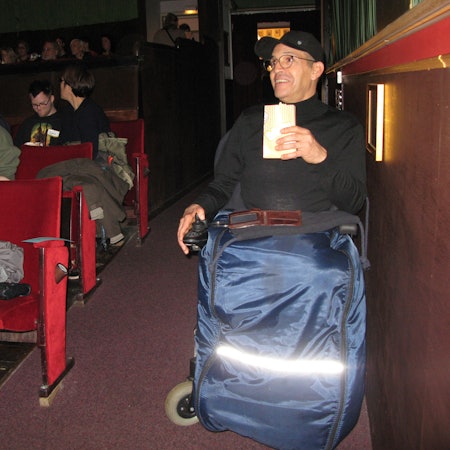 Ein Mann im Rollstuhl hat im Kino-Saal im Parkett seinen Platz eingenommen.