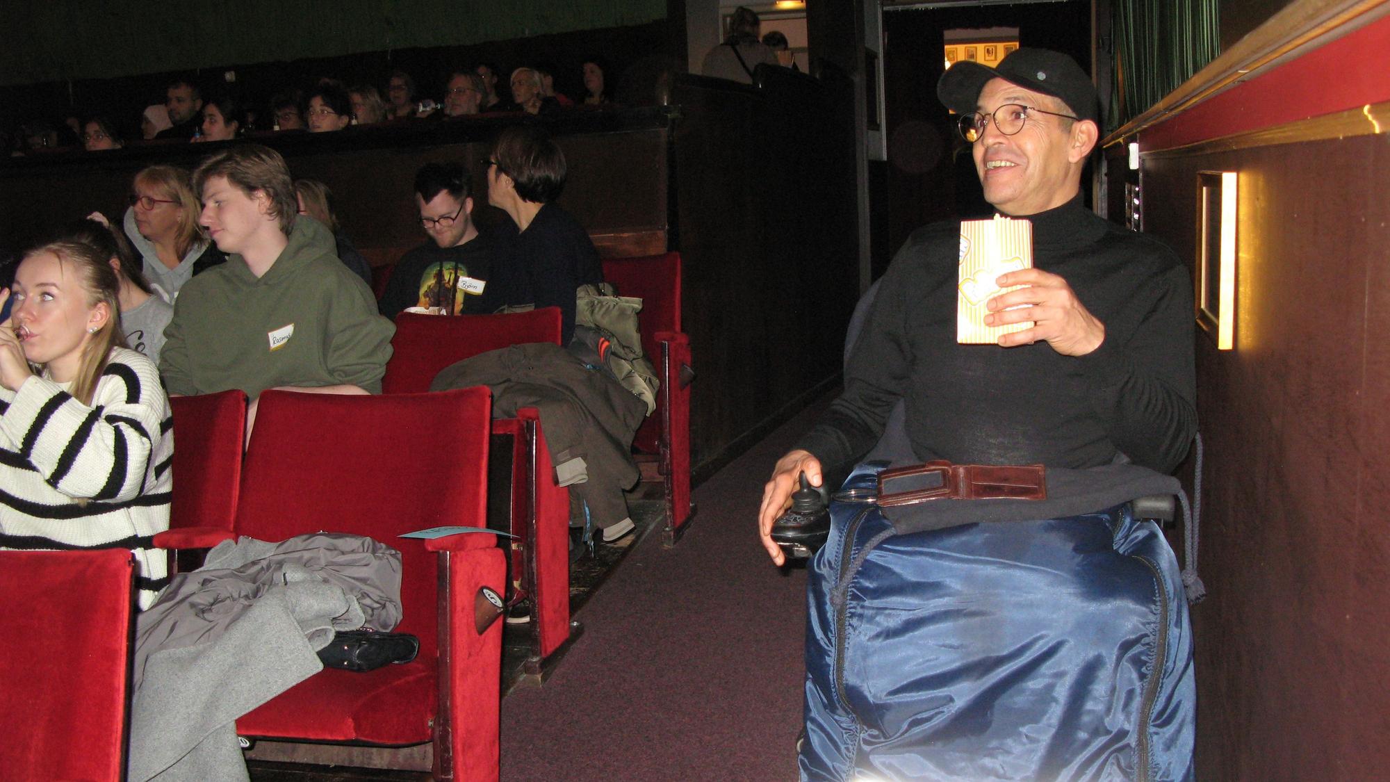 Ein Mann im Rollstuhl hat im Kino-Saal im Parkett seinen Platz eingenommen.