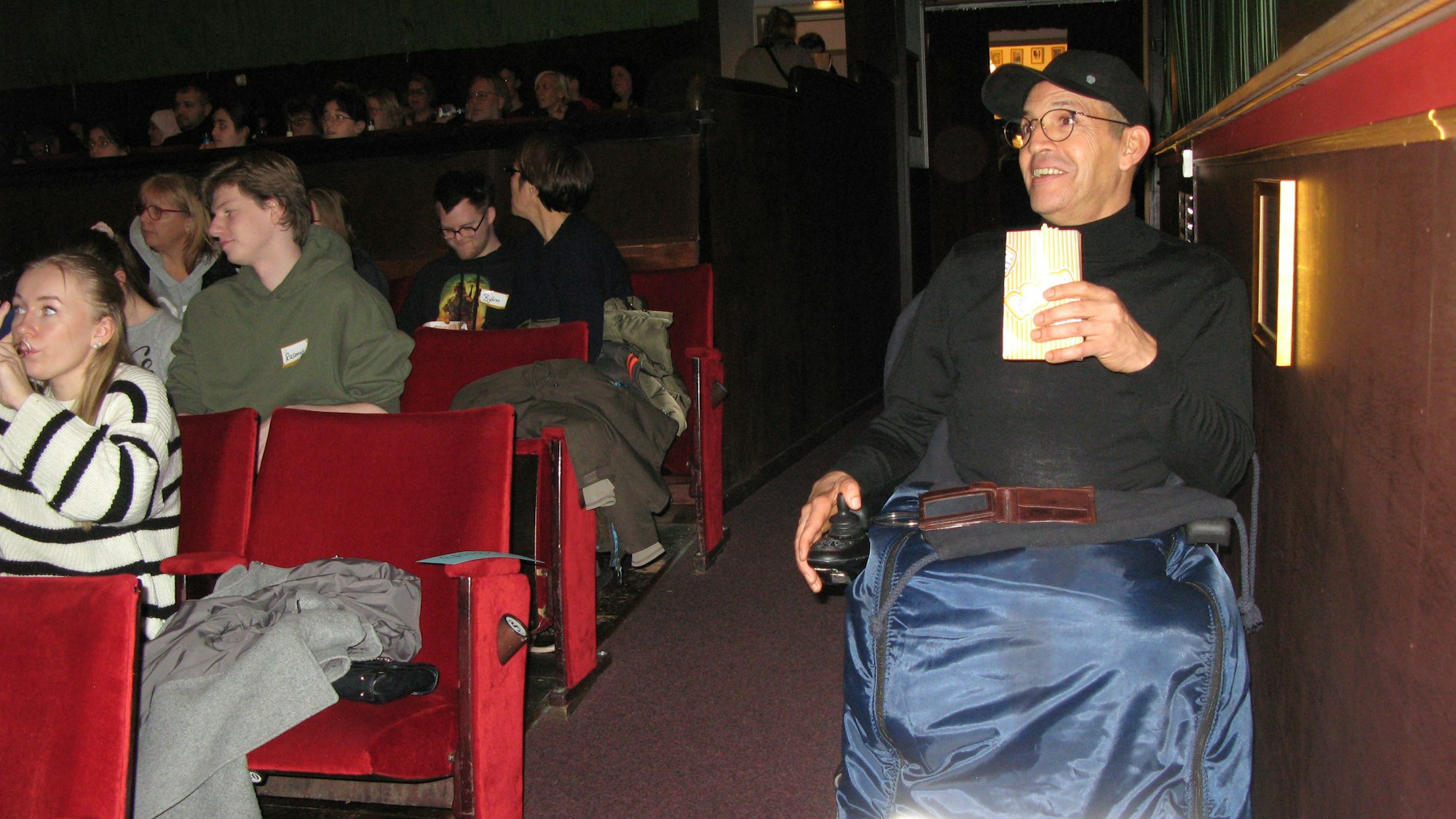 Ein Mann im Rollstuhl hat im Kino-Saal im Parkett seinen Platz eingenommen.