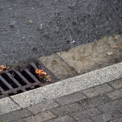 Regenwasser läuft während eines Gewitters durch einen Straßenablauf in die Kanalisation.