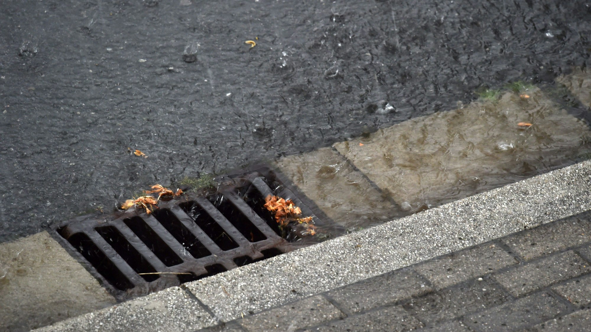 Regenwasser läuft während eines Gewitters durch einen Straßenablauf in die Kanalisation.