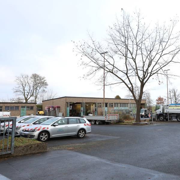 Auf dem Gelände des Baubetriebshofes in Oberpleis stehen mehrere Pkw und Lkw. An einem Gebäude im Hintergrund stehen Tore offen.