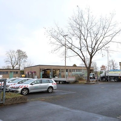 Auf dem Gelände des Baubetriebshofes in Oberpleis stehen mehrere Pkw und Lkw. An einem Gebäude im Hintergrund stehen Tore offen.