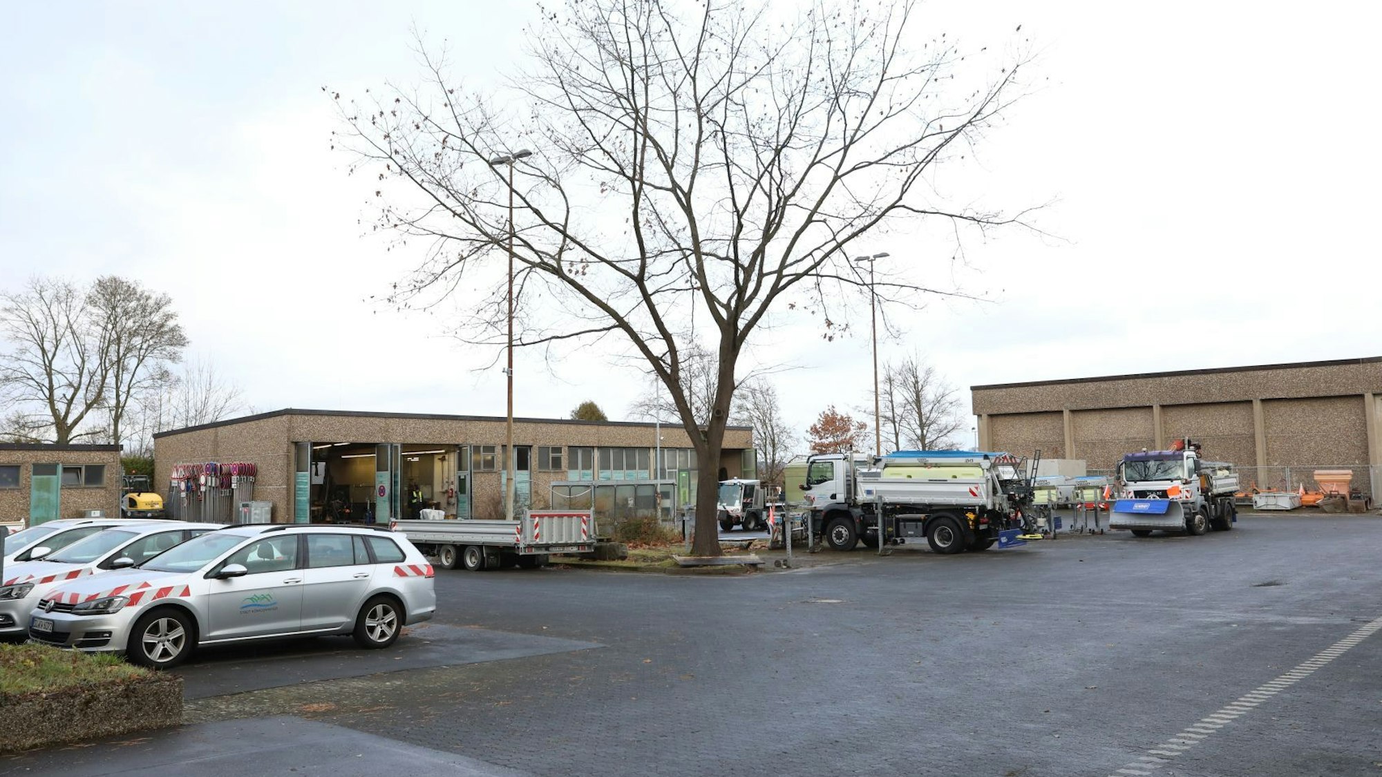 Auf dem Gelände des Baubetriebshofes in Oberpleis stehen mehrere Pkw und Lkw. An einem Gebäude im Hintergrund stehen Tore offen.
