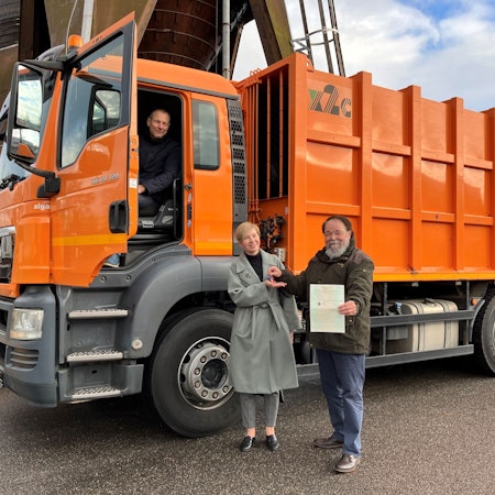 Bürgermeister Bernhard Marewski überreicht Schlüssel und Fahrzeugpapiere an Olesya Schmidt vom Verein Blau-Gelbes Kreuz. Beide stehen vor einem Müllfahrzeug. Im Fahrerhaus sitzt Wulf Riedel, Vorstand der Technischen Betrieben der Stadt Leverkusen.