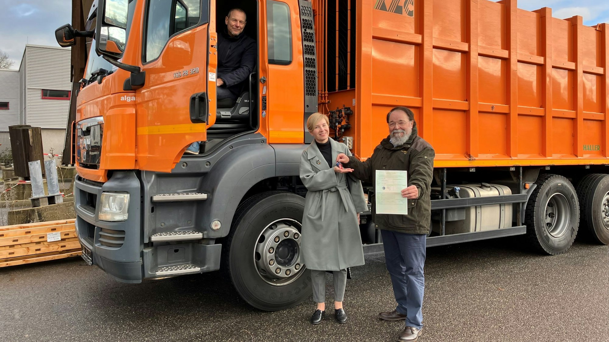 Bürgermeister Bernhard Marewski überreicht Schlüssel und Fahrzeugpapiere an Olesya Schmidt vom Verein Blau-Gelbes Kreuz. Beide stehen vor einem Müllfahrzeug. Im Fahrerhaus sitzt Wulf Riedel, Vorstand der Technischen Betrieben der Stadt Leverkusen.