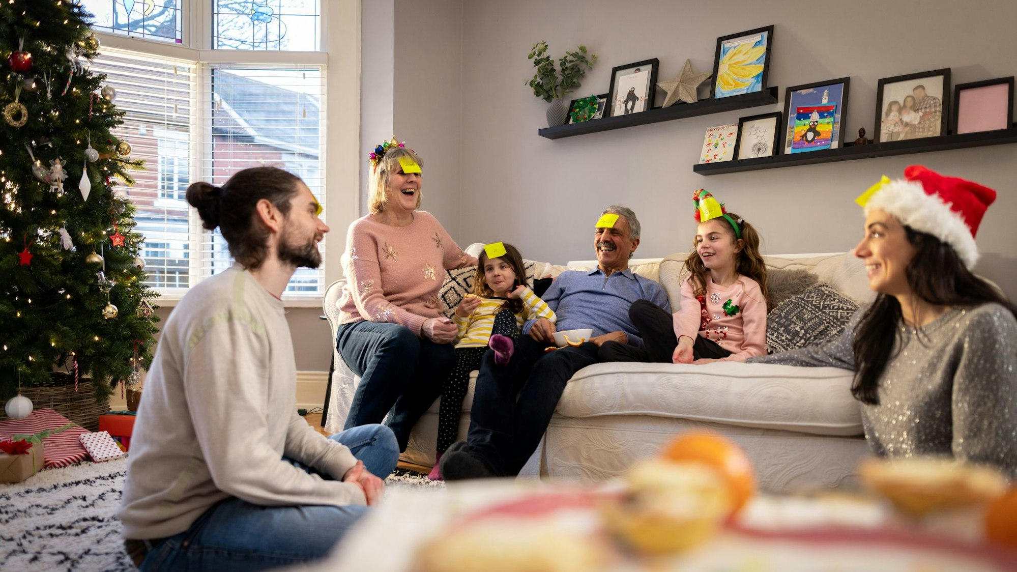 Sechs Menschen am Tannenbaum mit Zettel auf der Stirn.