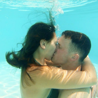 Ein junger Mann und eine junge Frau küssen sich unter Wasser in einem Swimmingpool.