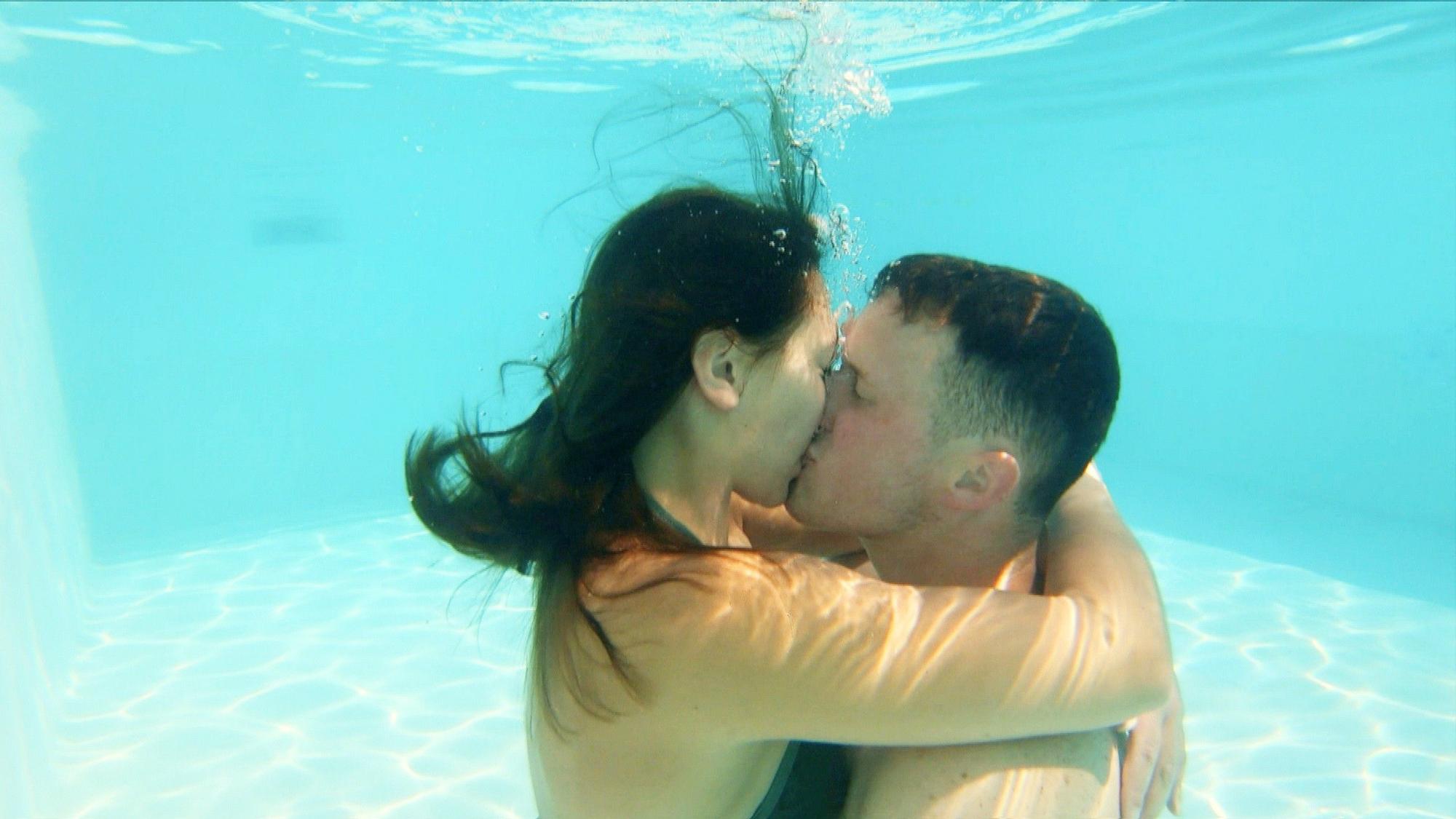 Ein junger Mann und eine junge Frau küssen sich unter Wasser in einem Swimmingpool.
