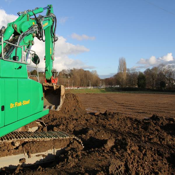 Ein grüner Bagger vor einem unbebautem Feld.
