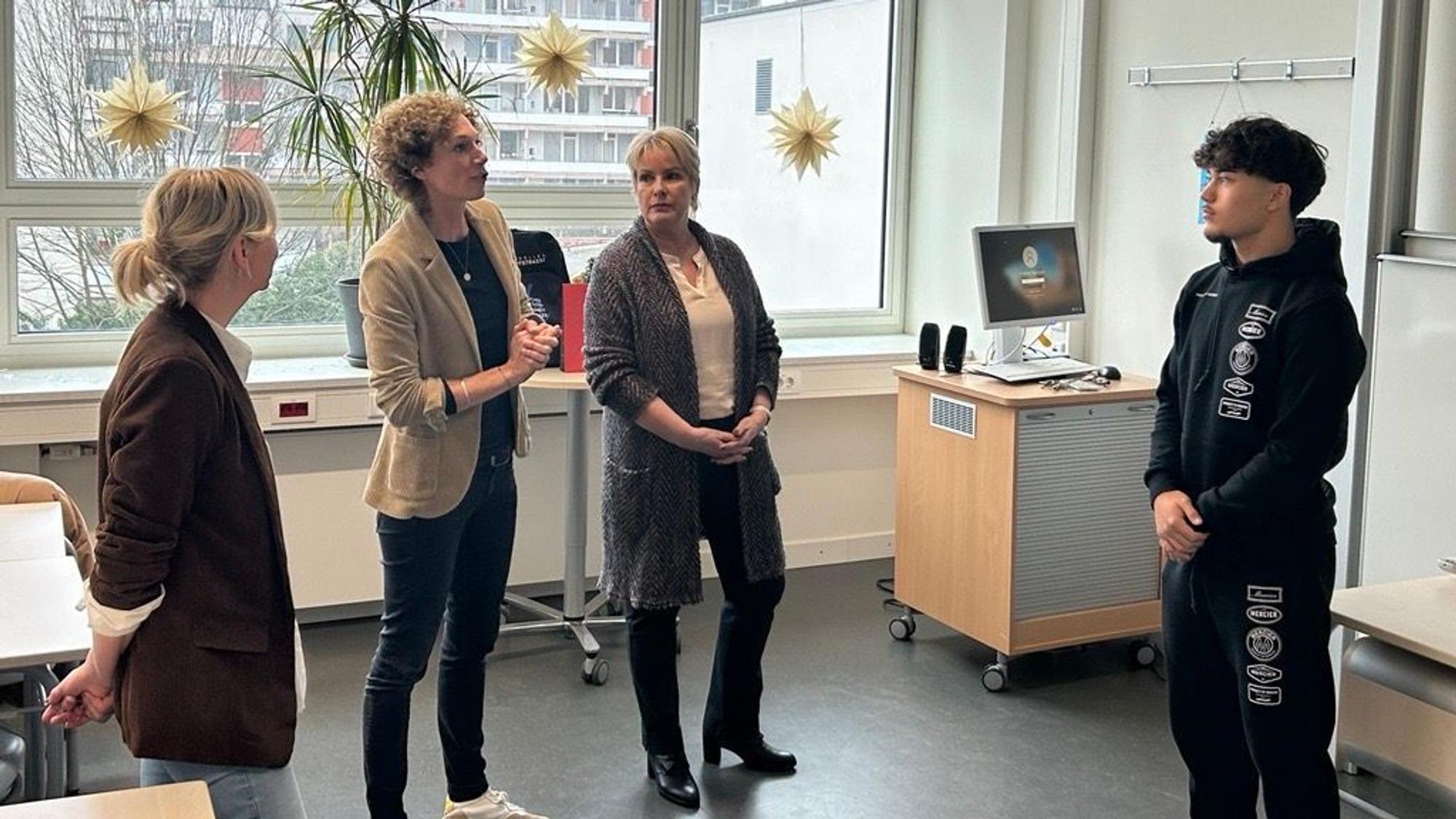 Drei Frauen stehen vor einem Jugendlichen in einem Klassenzimmer.
