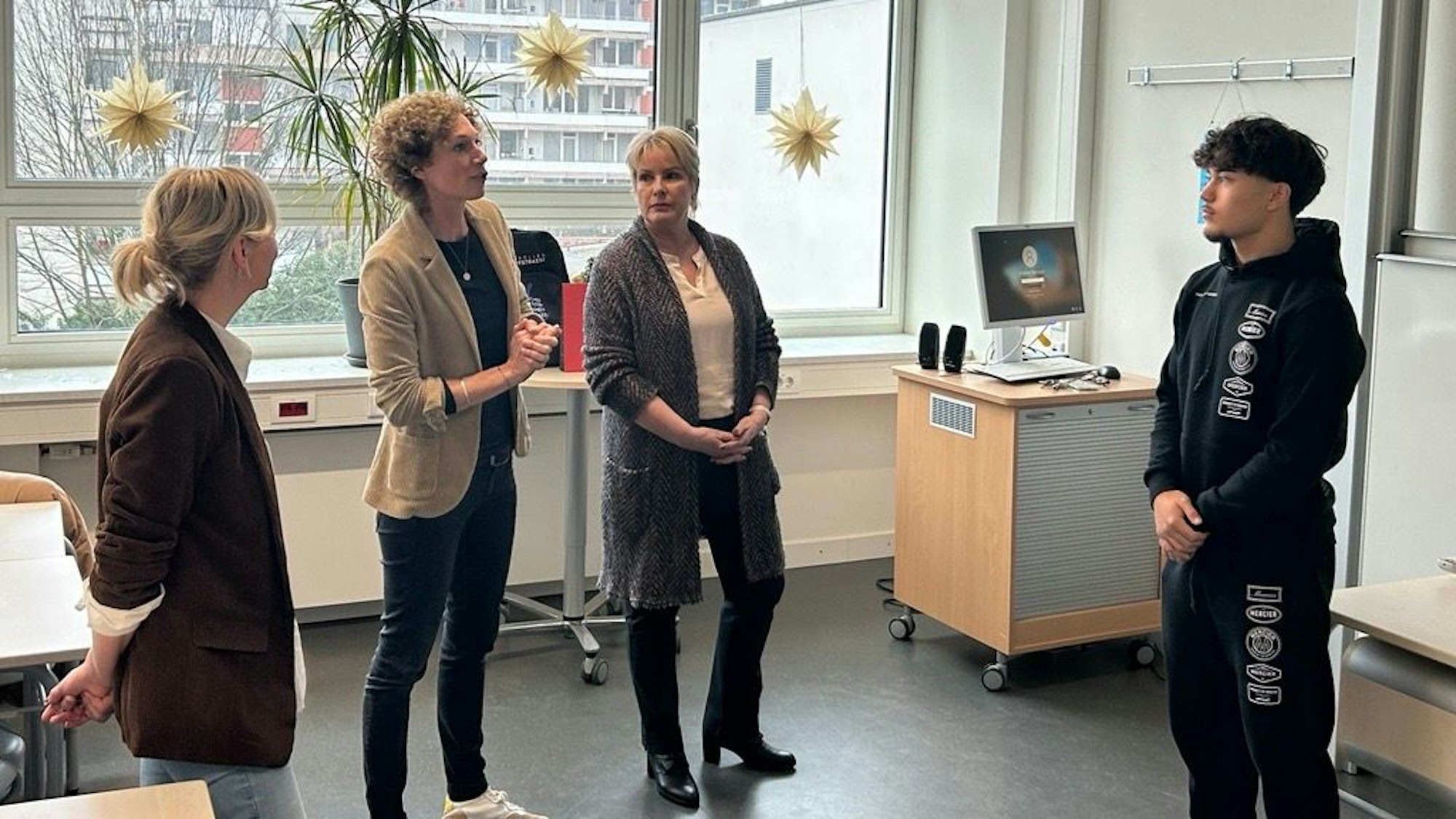 Drei Frauen stehen vor einem Jugendlichen in einem Klassenzimmer.