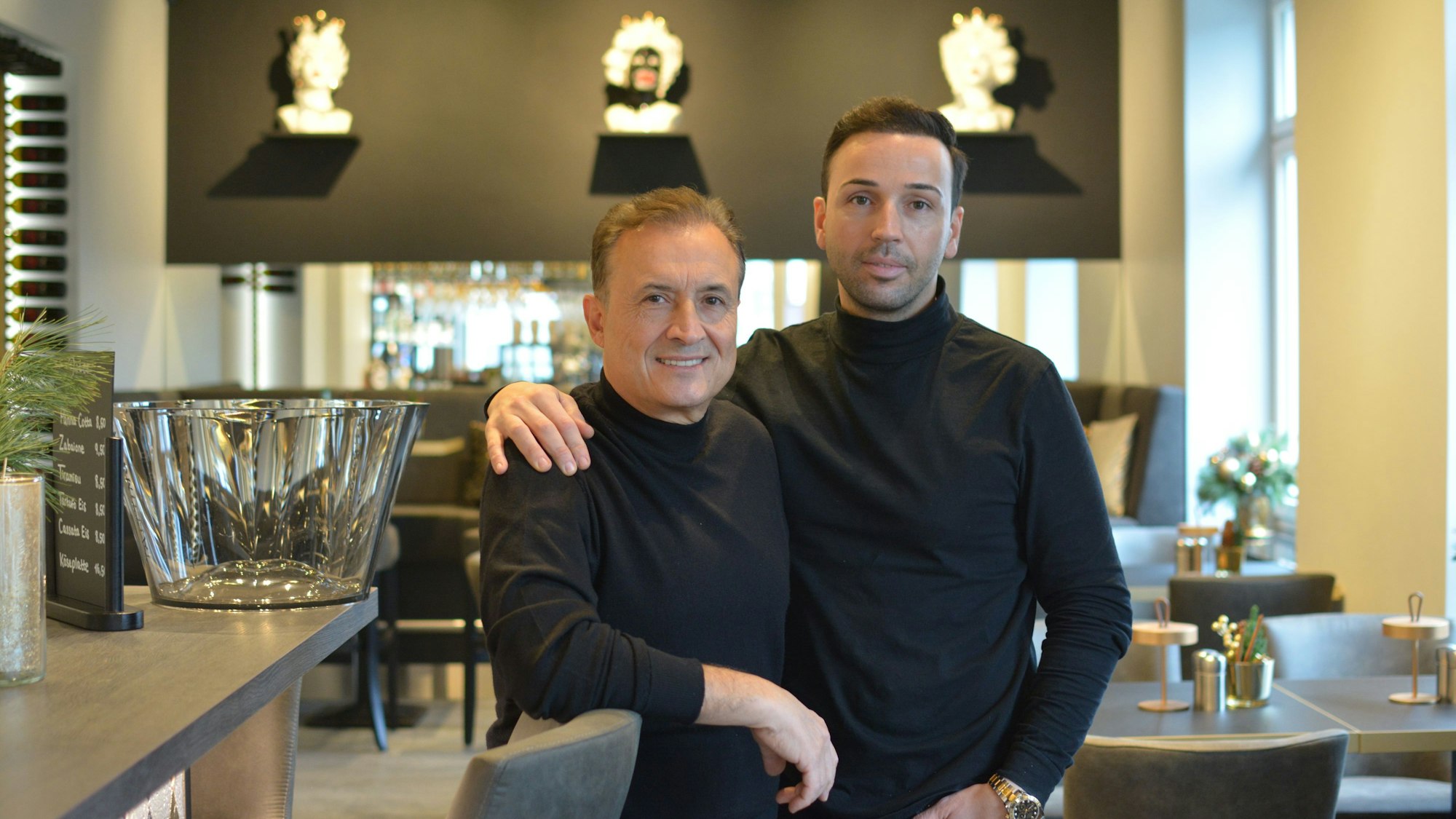 Zwei Männer stehen gemeinsam in einem Restaurant und schauen in die Kamera.