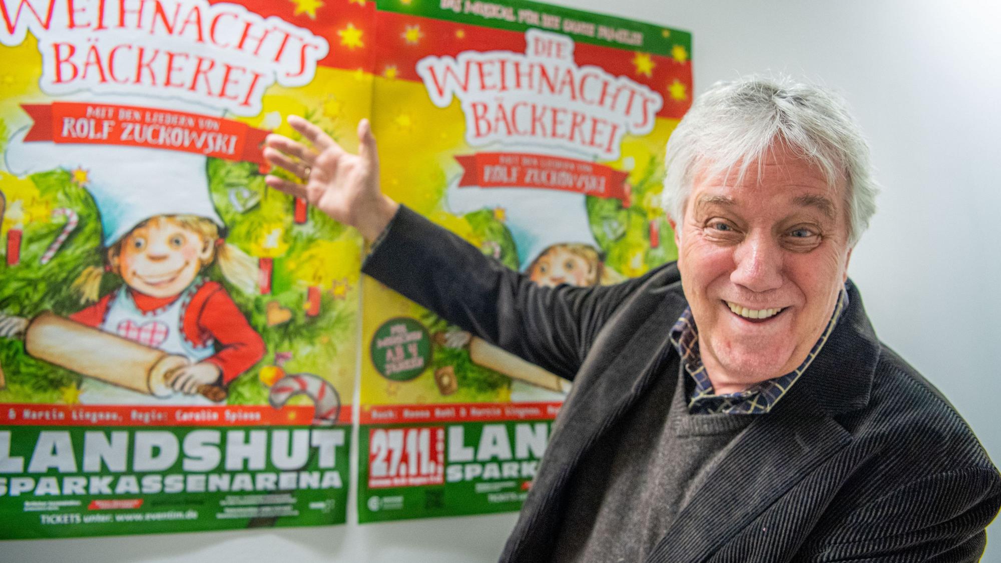 Rolf Zuckowski, Liedermacher, zeigt auf Poster seines Musicals "Die Weihnachtsbäckerei"