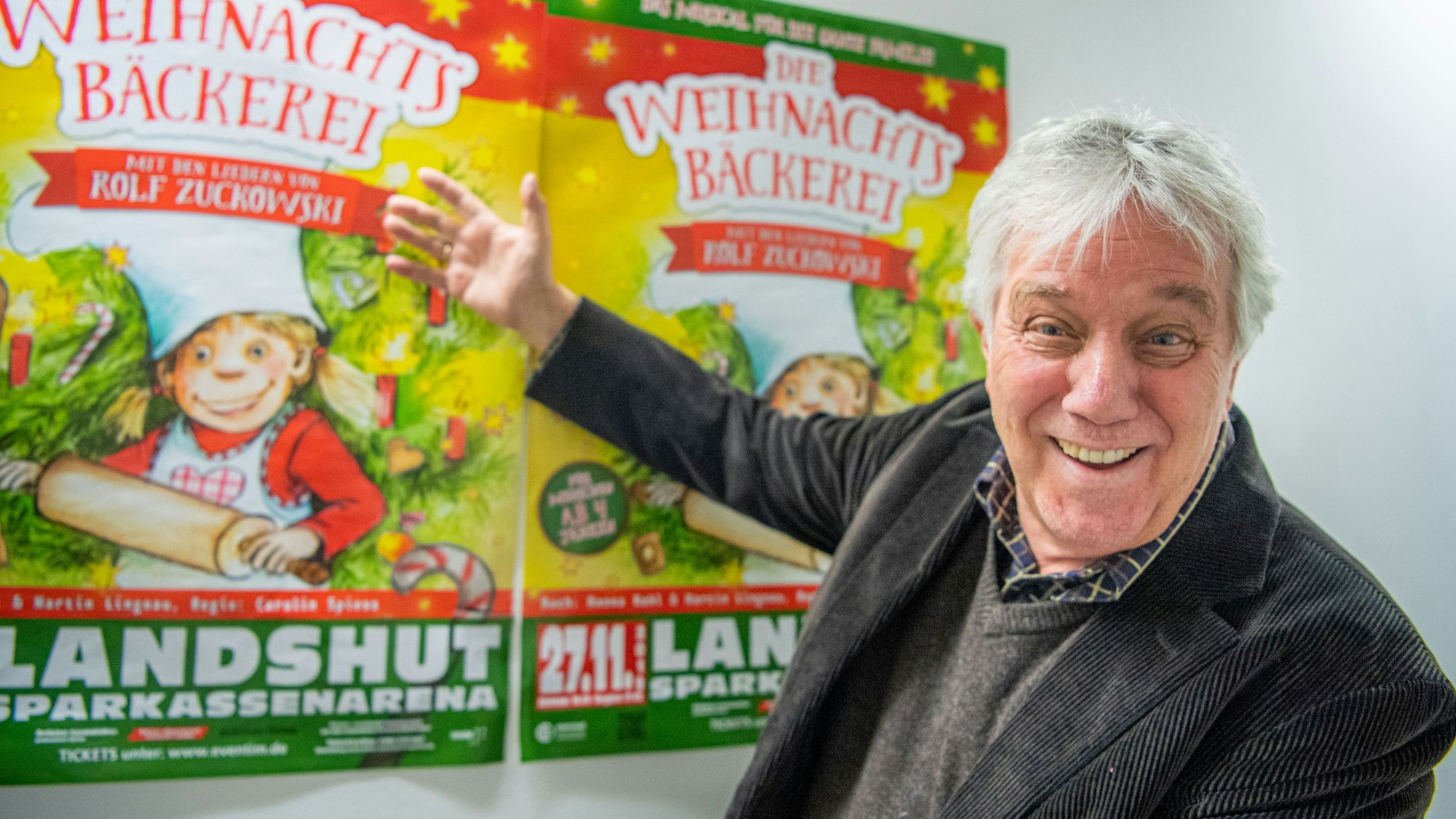 Rolf Zuckowski, Liedermacher, zeigt auf Poster seines Musicals "Die Weihnachtsbäckerei"