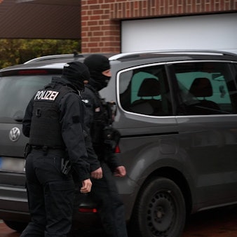 Vermummte Einsatzkräfte stehen vor einem Wohnhaus und Autos.