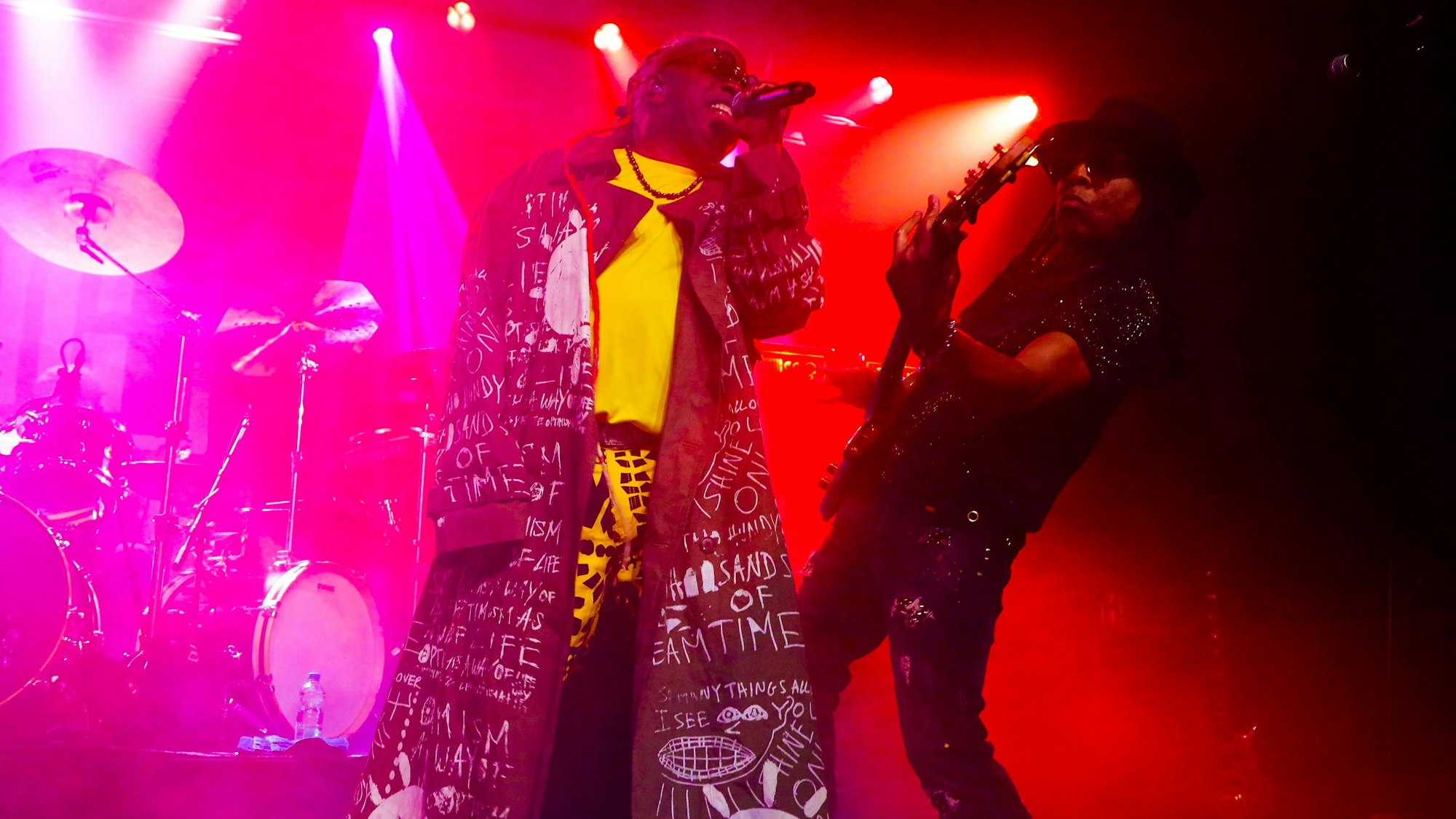 13.12.2023, Köln: Konzert von Living Colour in der Kantine: Sänger Corey Glover trägt einen Mantel mit Motiven von Jean-Michel Basquiat über einem gelben T-Shirt. Bassist Douglas Wimbish ist ganz in schwarz mit Hut.