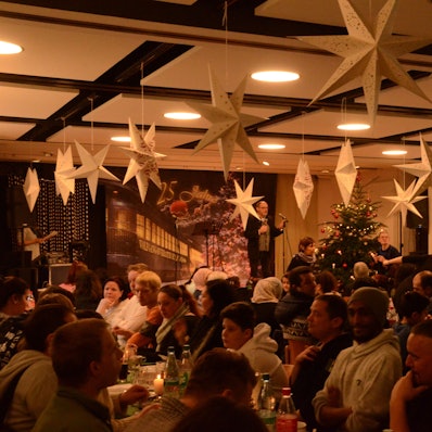 Menschen sitzen an Tischen, über ihnen hängen Papiersterne.
