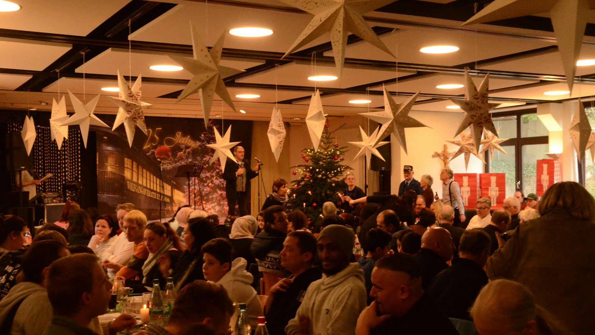 Menschen sitzen an Tischen, über ihnen hängen Papiersterne.
