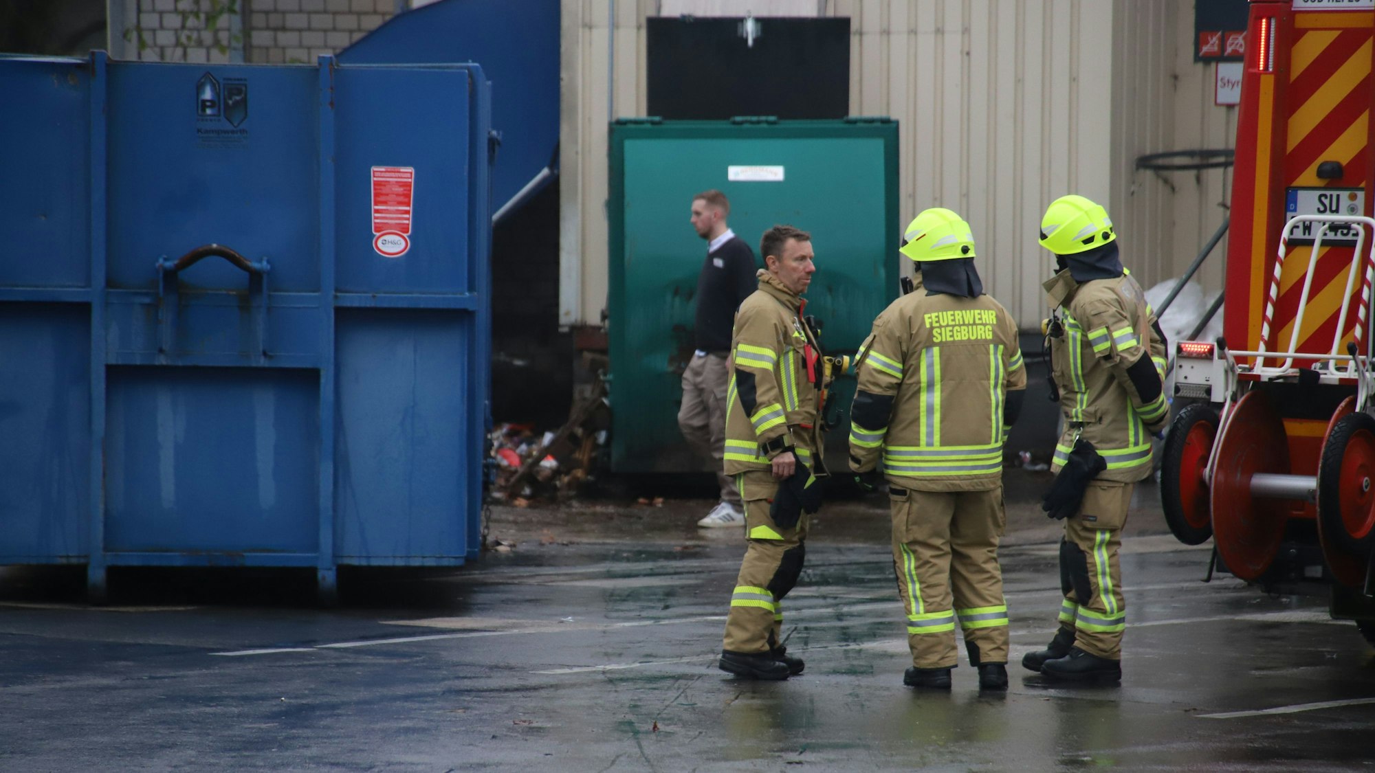 Feuerwehrleute stehen vor einer Müllpresse.