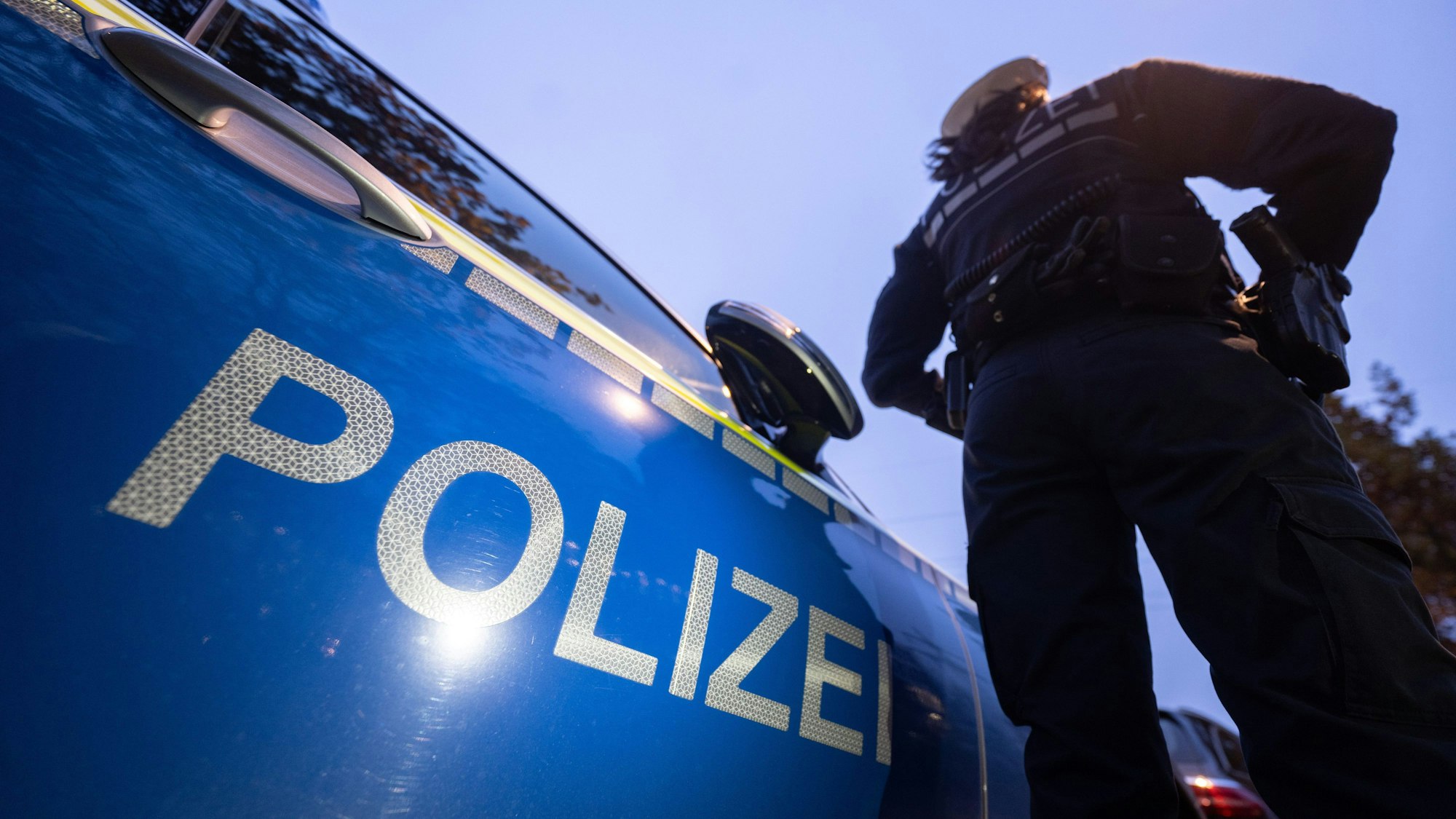 ARCHIV - 30.11.2023, Baden-Württemberg, Stuttgart: Eine Polizistin steht im Rahmen eines Fototermins neben einem Polizeifahrzeug (gestellte Szene).