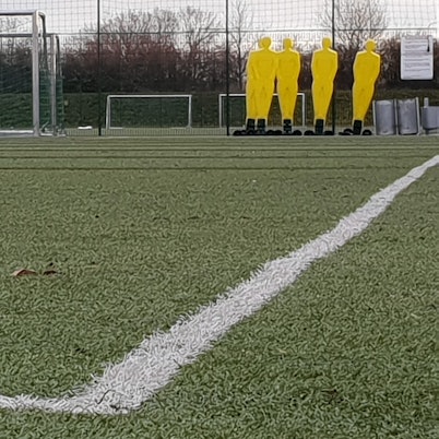 Ein Kunstrasenplatz mit weißer Seitenlinie, Figuren und Toren im Hintergrund.
