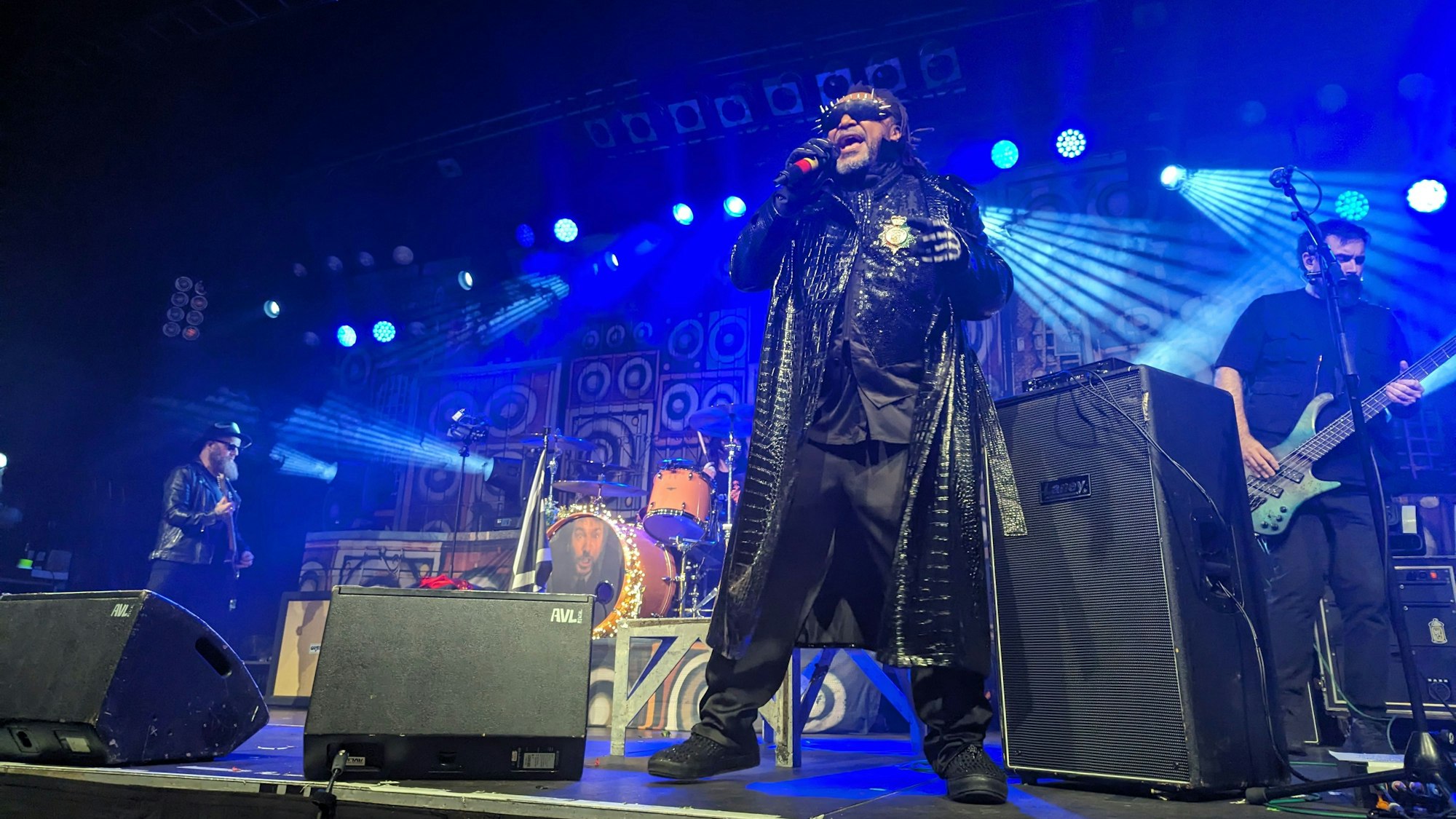 Benji Webbe steht mit schwarzem Mantel auf der Bühne und singt