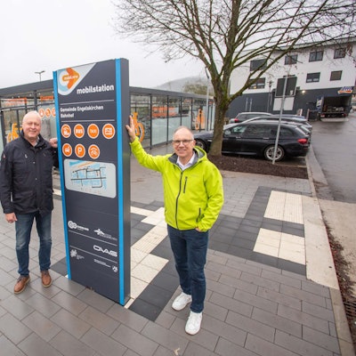 Zwei Männer posieren an einer Bushaltestelle.