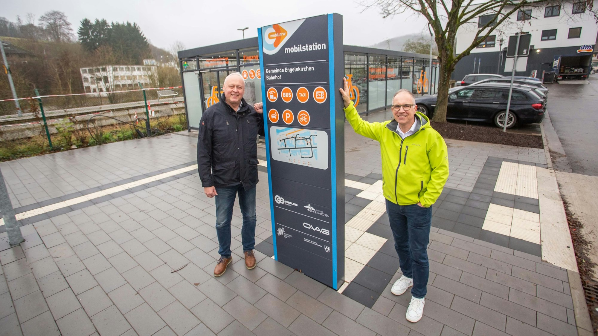 Zwei Männer posieren an einer Bushaltestelle.