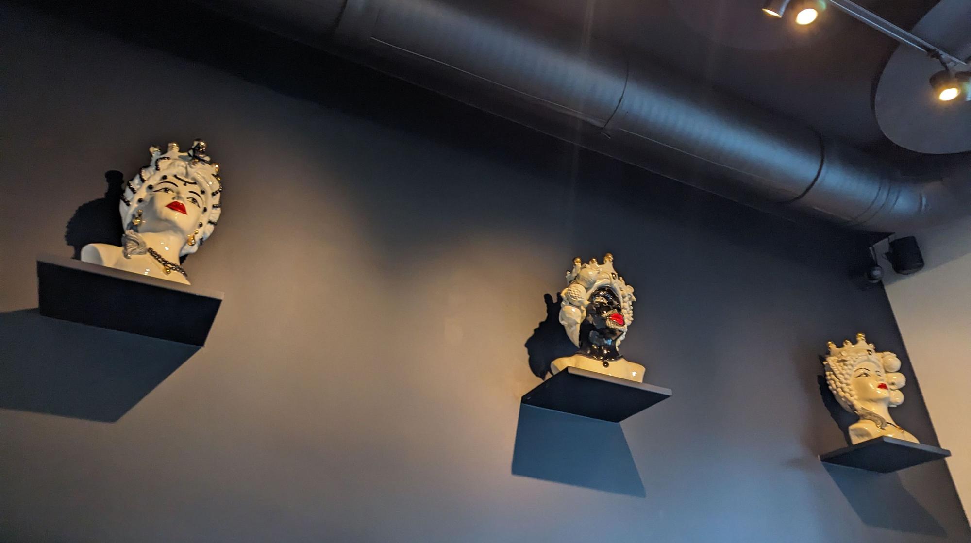 Büsten aus Keramik hängen an einer schwarzen Wand.