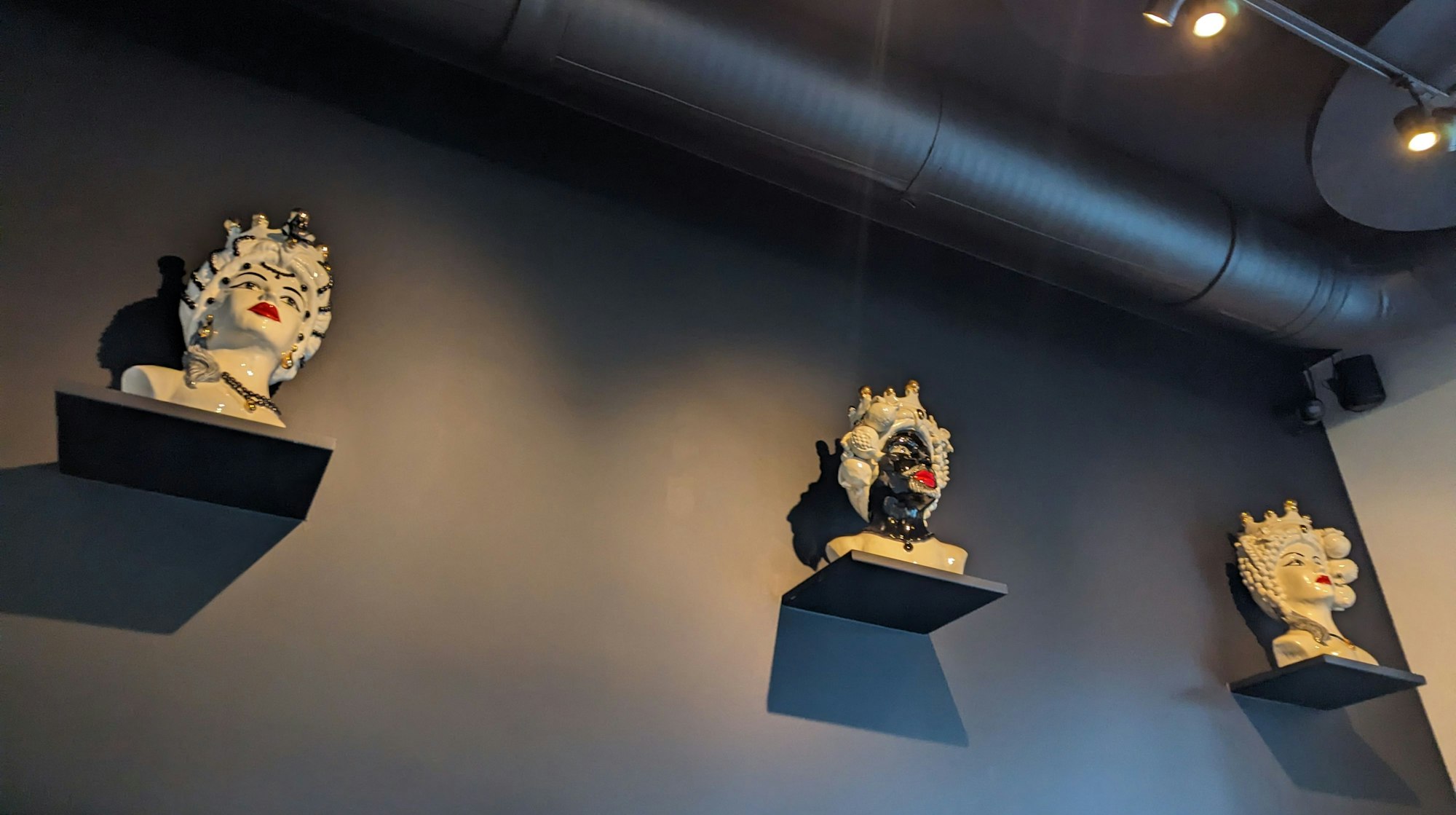 Büsten aus Keramik hängen an einer schwarzen Wand.