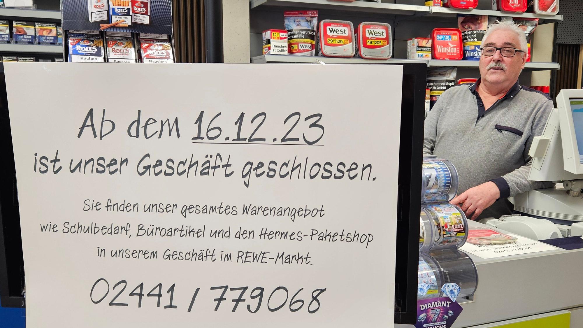 Hans-Dieter Pütz steht hinter einem Schild, das die Schließung des Geschäfts ankündigt, am Tresen.