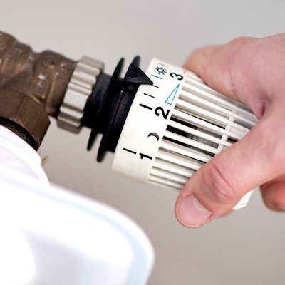 Eine Frau dreht am Thermostat eines Heizkörpers.