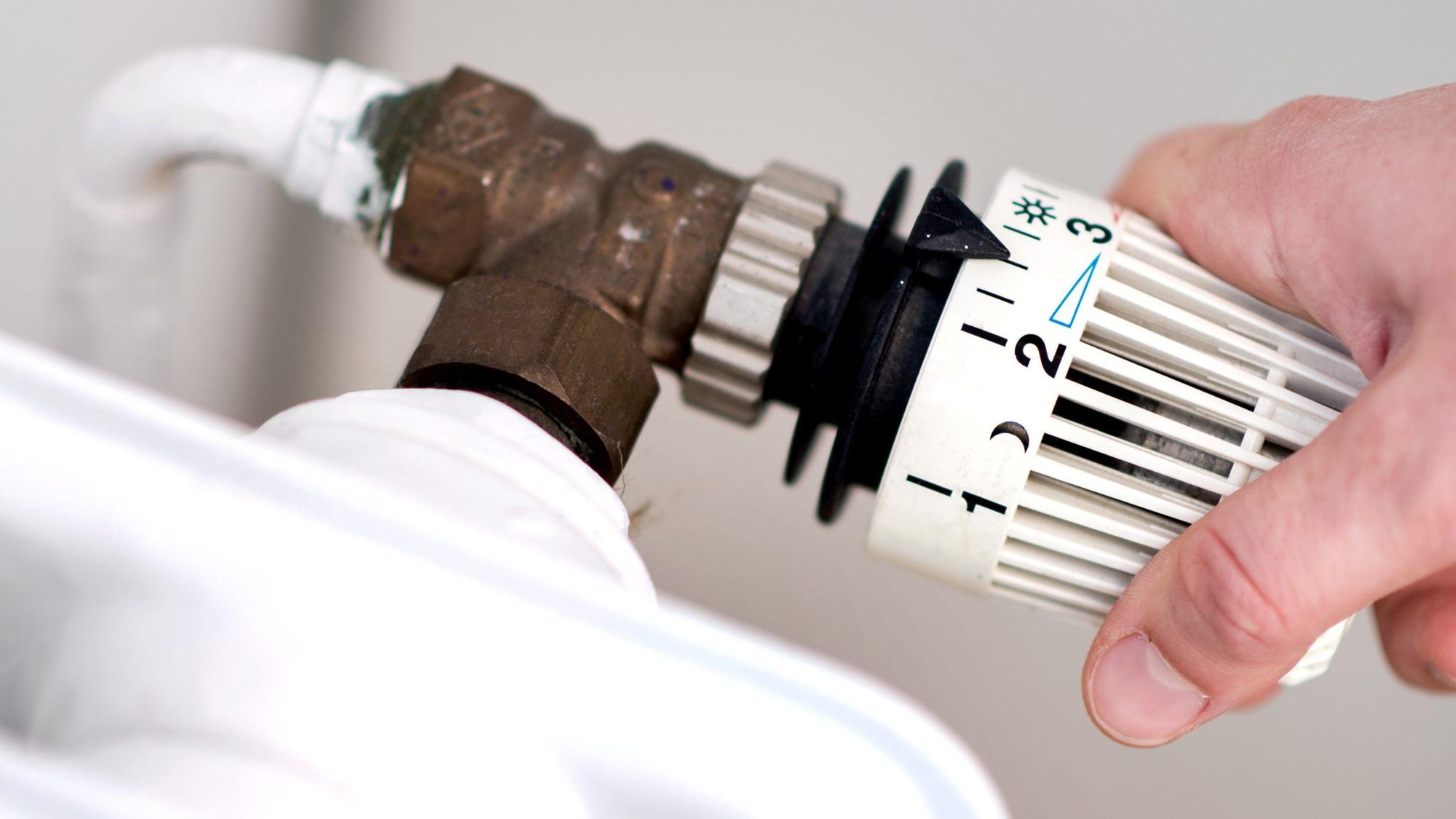 Eine Frau dreht am Thermostat eines Heizkörpers.