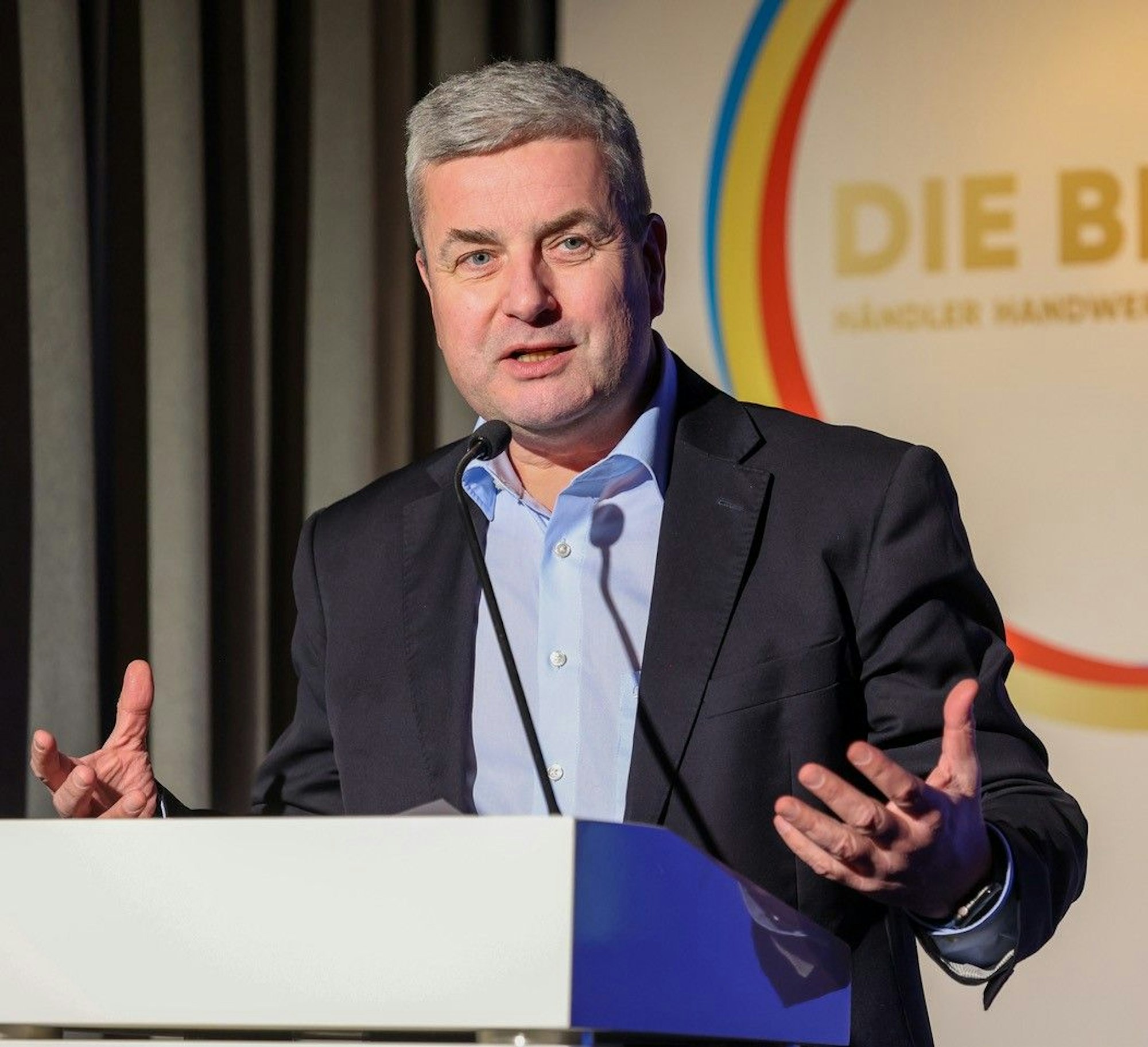 Auf dem Bild ist das Portrait eines Mannes an einem Rednerpult zu sehen.
