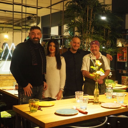 Drei Männer und eine Frau stehen an einem gedeckten Tisch.