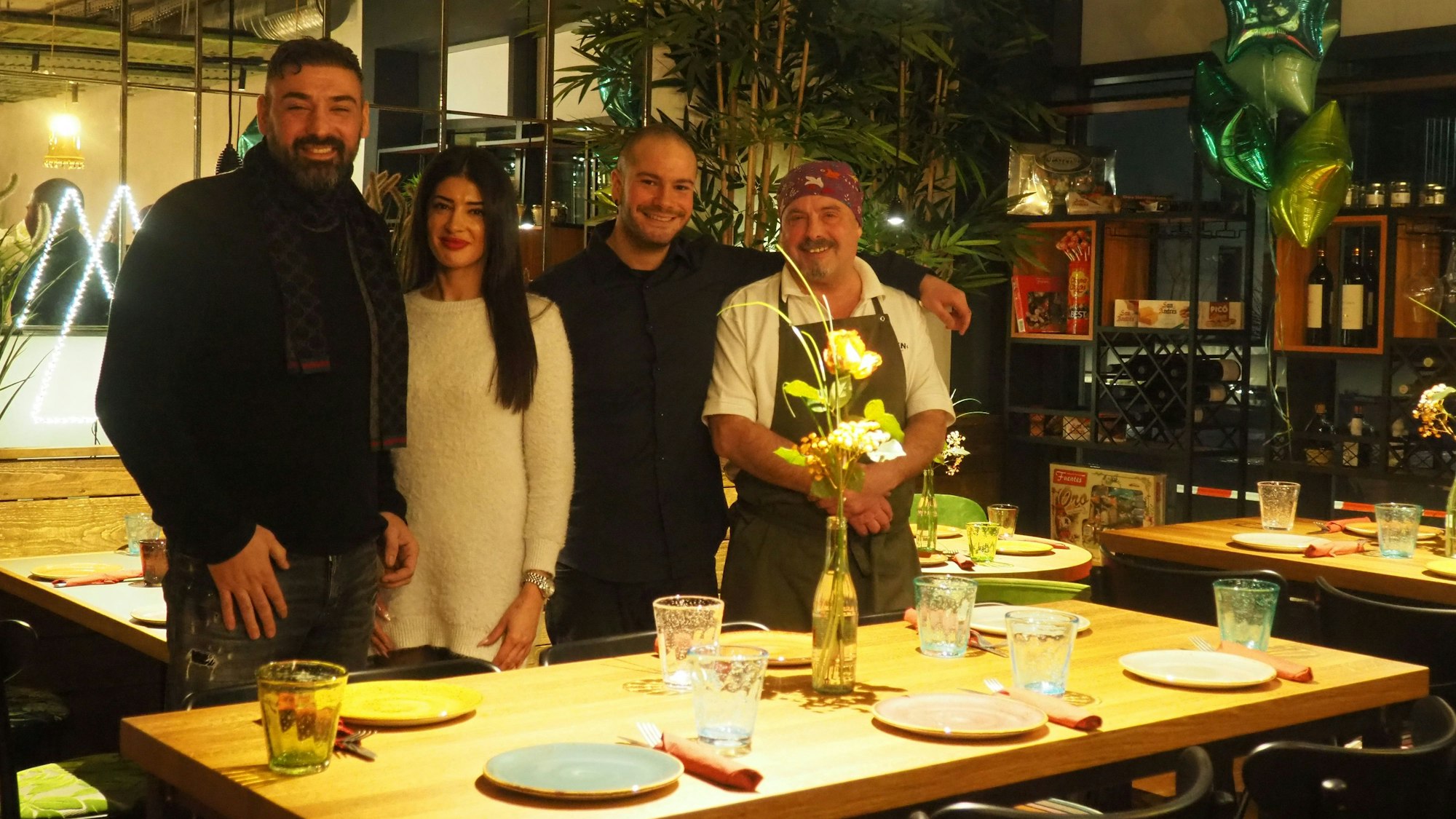 Drei Männer und eine Frau stehen an einem gedeckten Tisch.