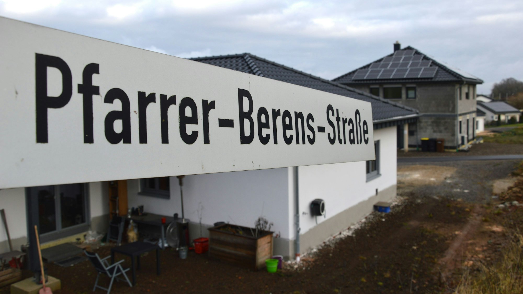 Blick auf ein Straßenschild der Pfarrer-Berens-Straße mit Wohnhäusern im Hintergrund.