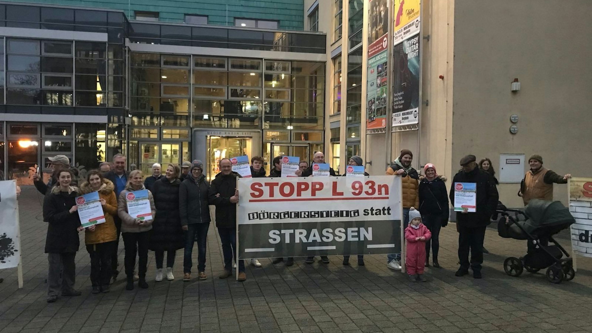 Menschen stehen vor einem großen Gebäude und halten Plakate und Transparente gegen einen Straßenbau.